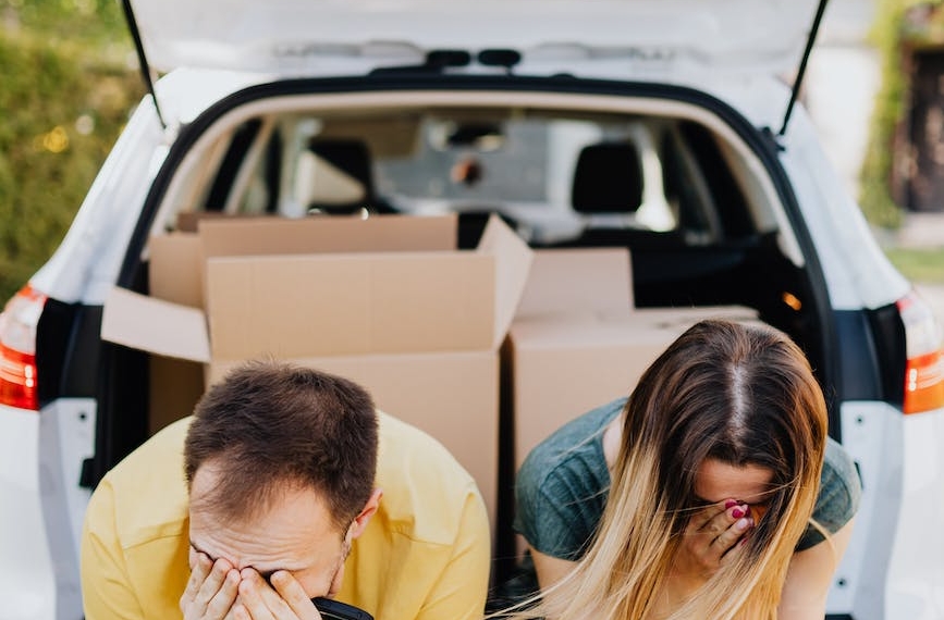 tired couple sitting on car luggage boot