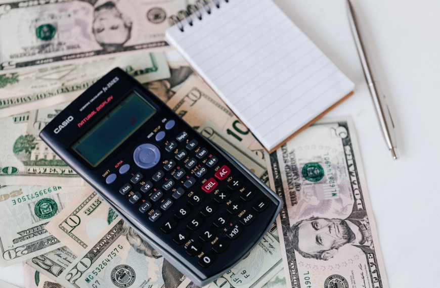 calculator and notepad placed on usa dollars stack