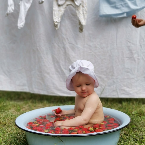 a baby bathing in a basin filled with strawberries