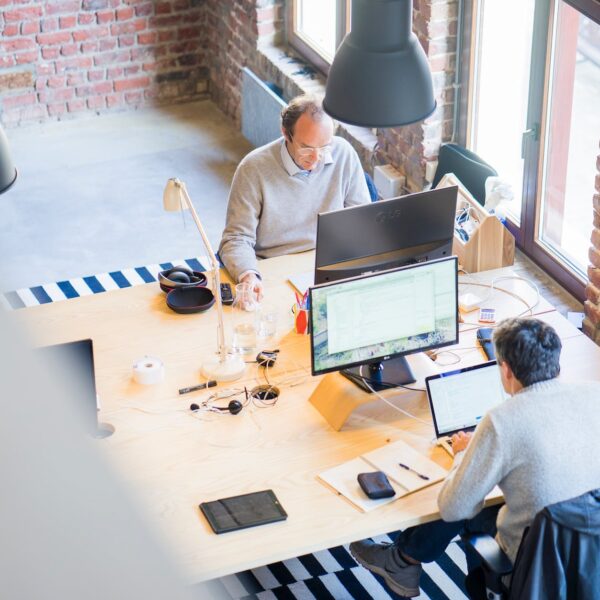 two men sitting facing on flat screen monitors