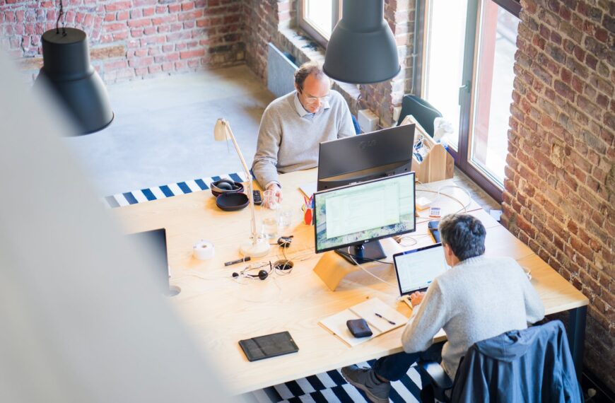 two men sitting facing on flat screen monitors