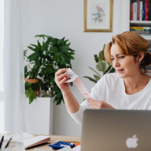 woman sitting behind a desk using laptop and looking at items on a receipt