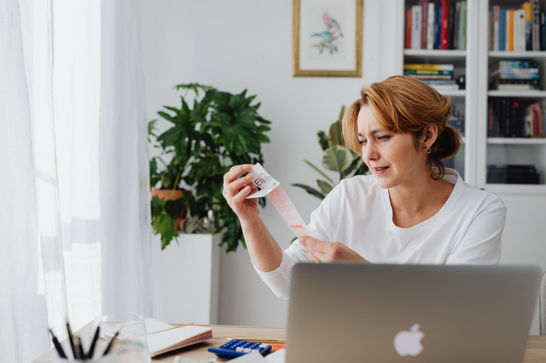 woman sitting behind a desk using laptop and looking at items on a receipt