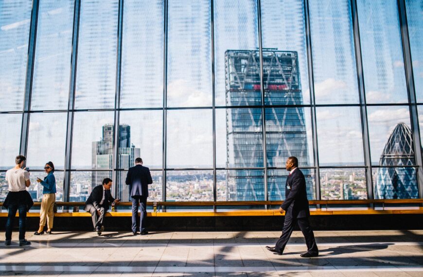 man walking on sidewalk near people standing and sitting beside curtain wall building
