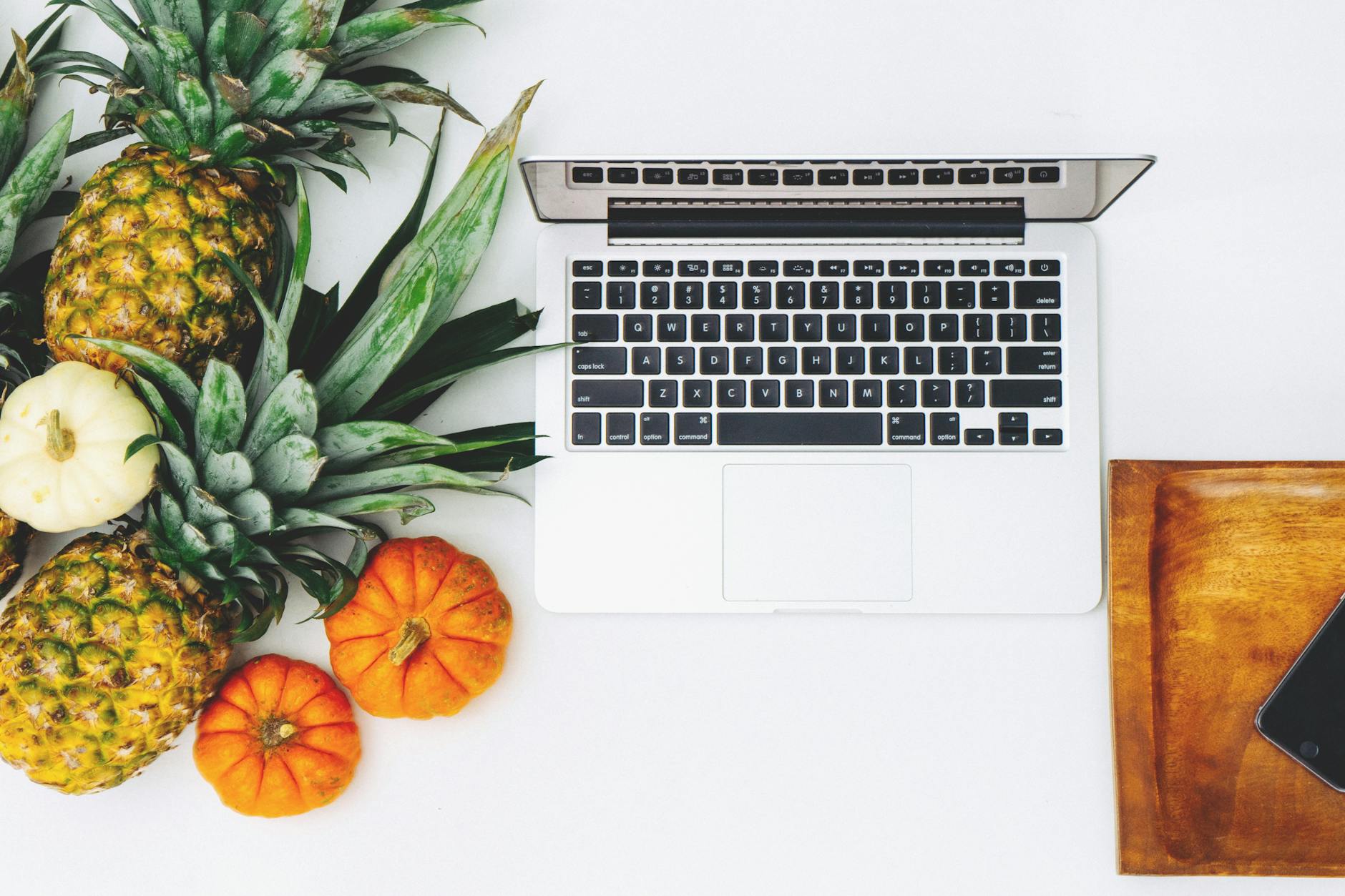 white macbook near pineapple and pumpkin