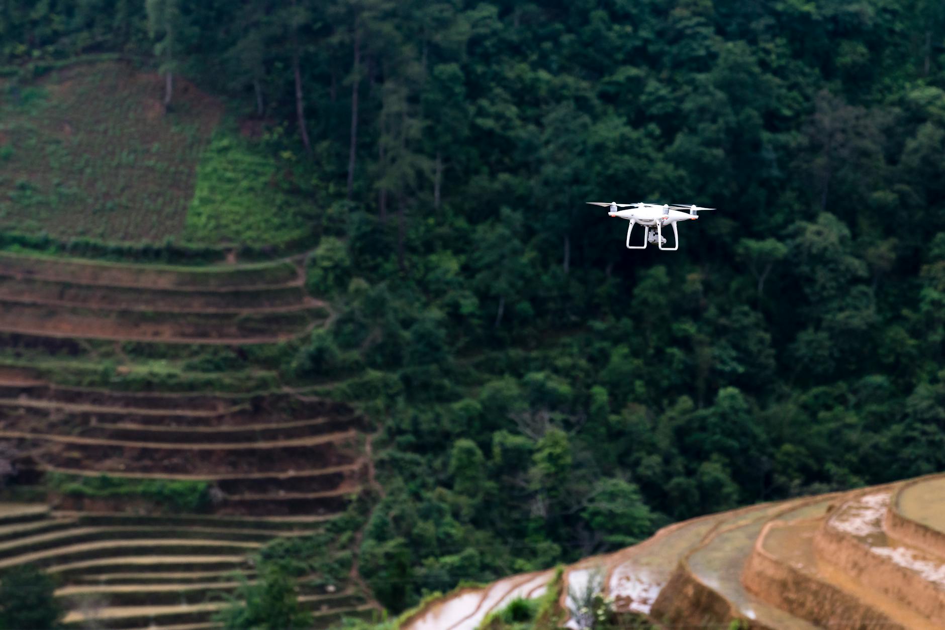 white drone flying above trees