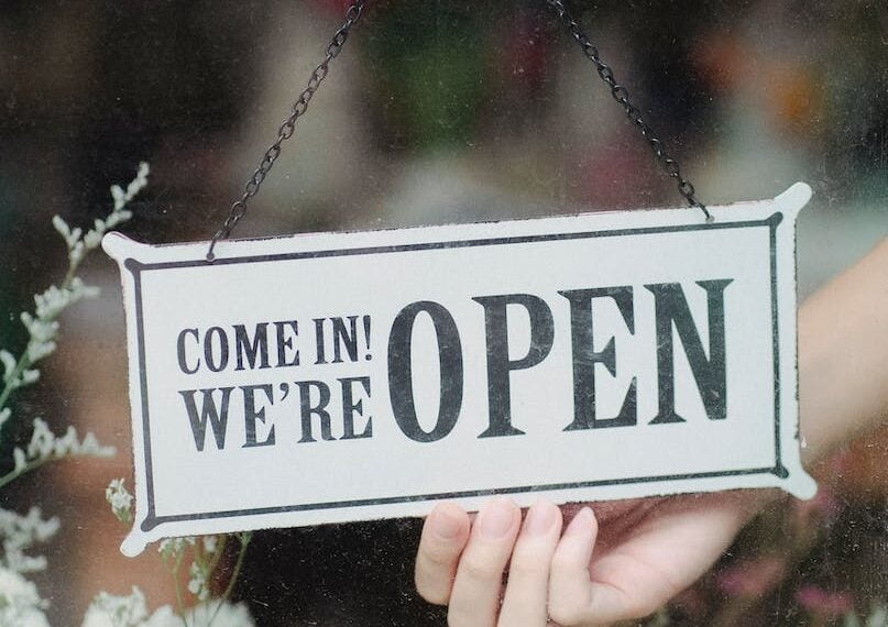 crop faceless person turning shop signboard hanging on glass wall