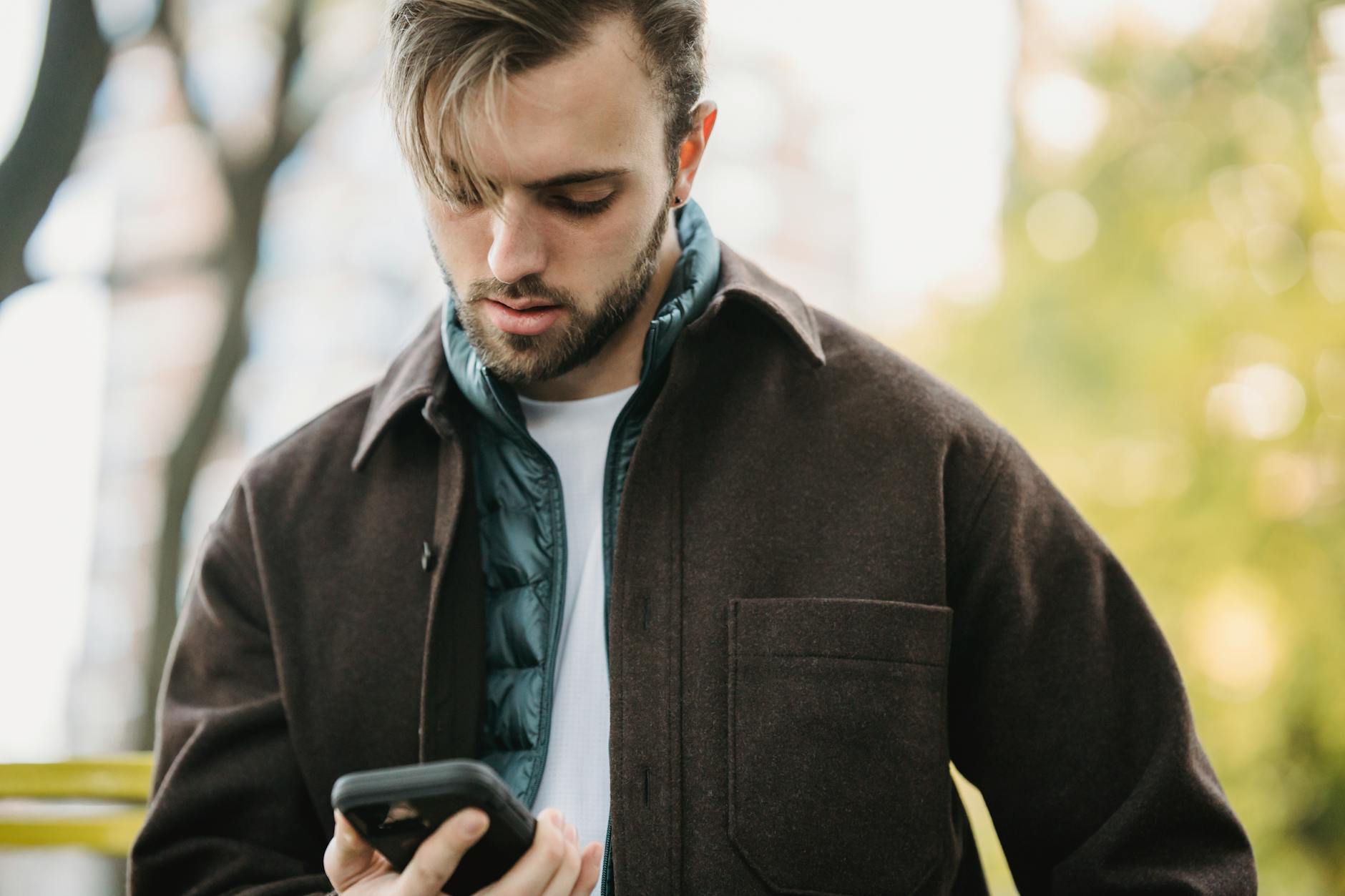 young hipster looking at smartphone screen in park