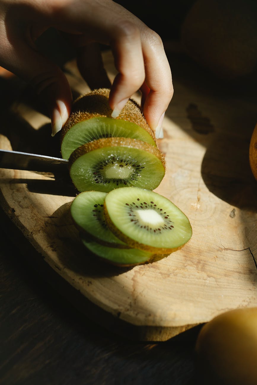 woman cutting ripe kiwi on chopping board in sunshine